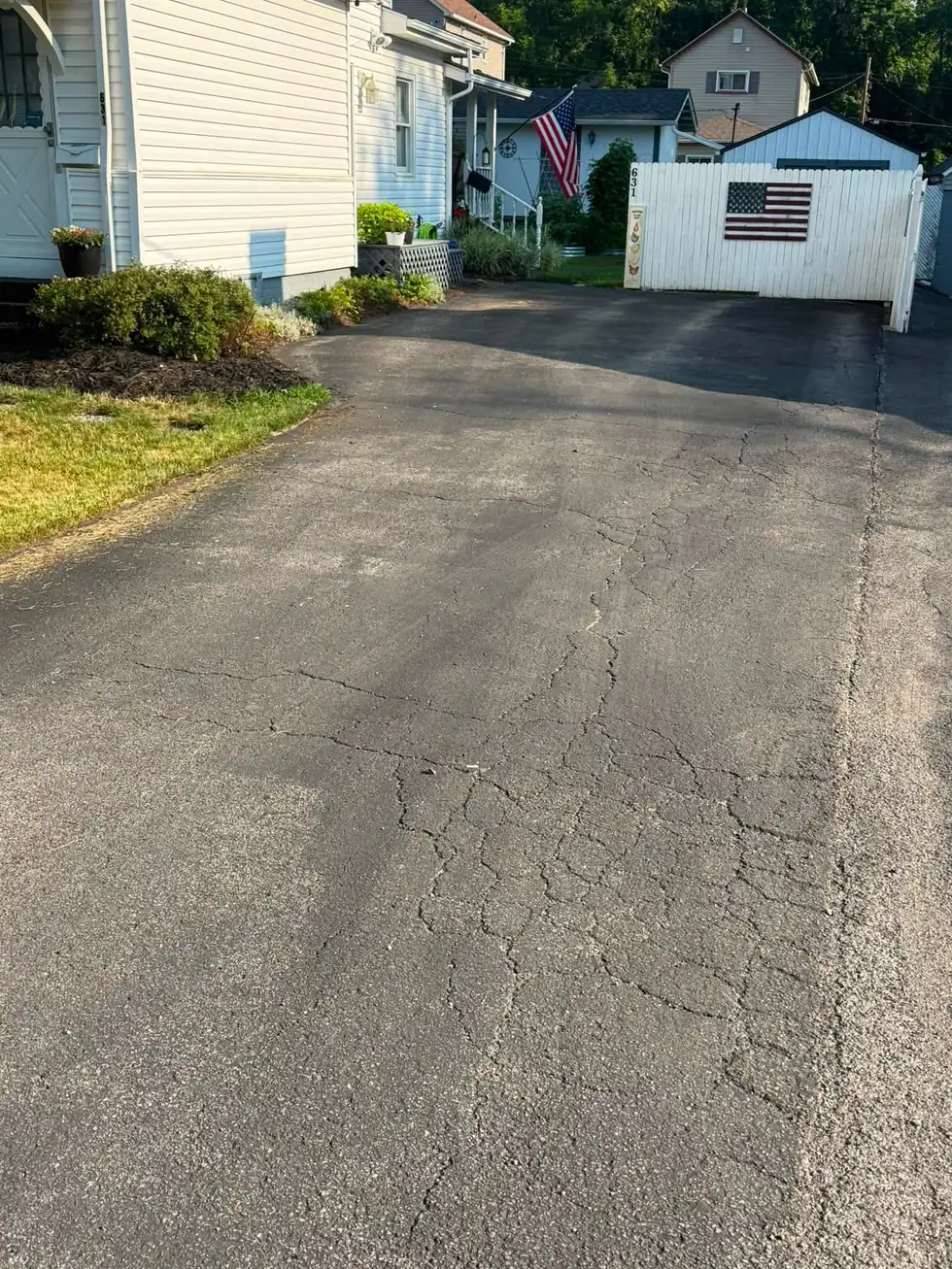 Close view of a weathered asphalt driveway with open cracks running across the surface before crack filling