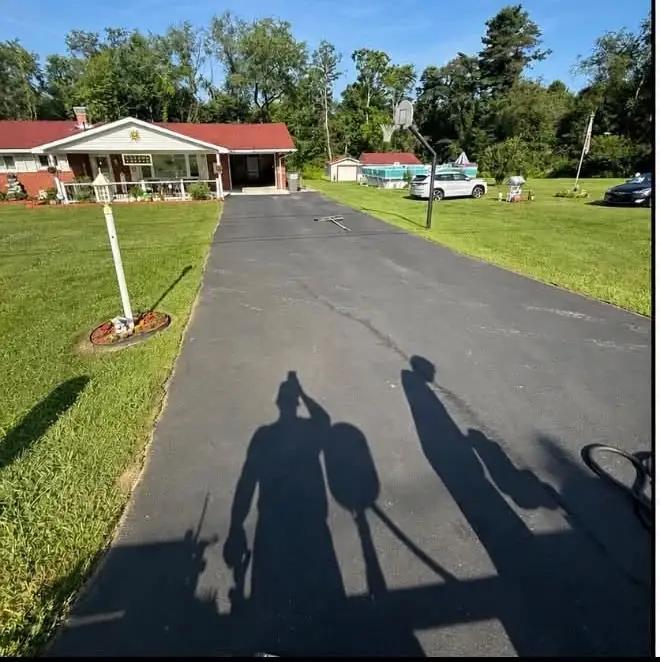 A long driveway running up to a ranch house with a red roof, grey and worn before sealing