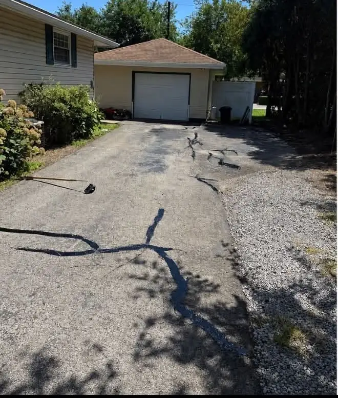 A cracked driveway leading to a detached garage before sealcoating
