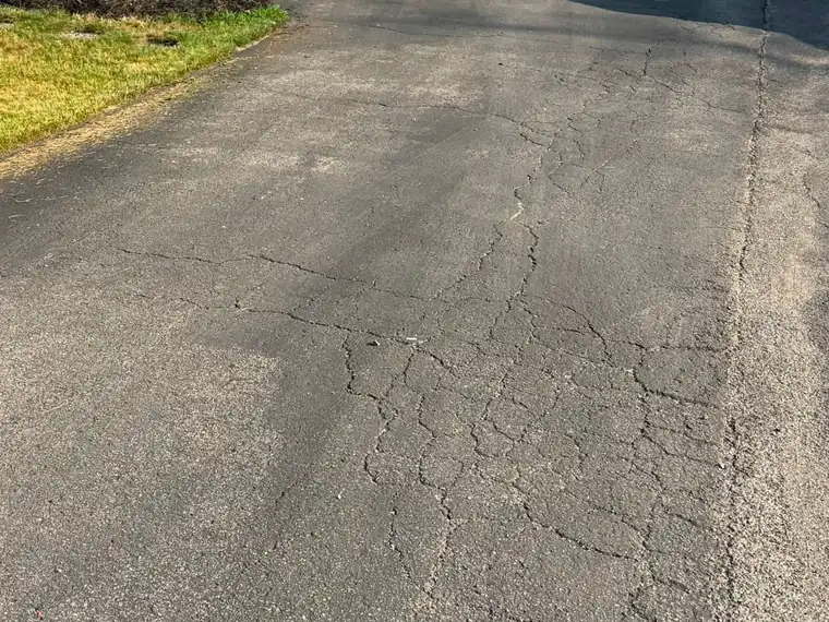 Close view of a badly cracked and faded asphalt driveway before repair