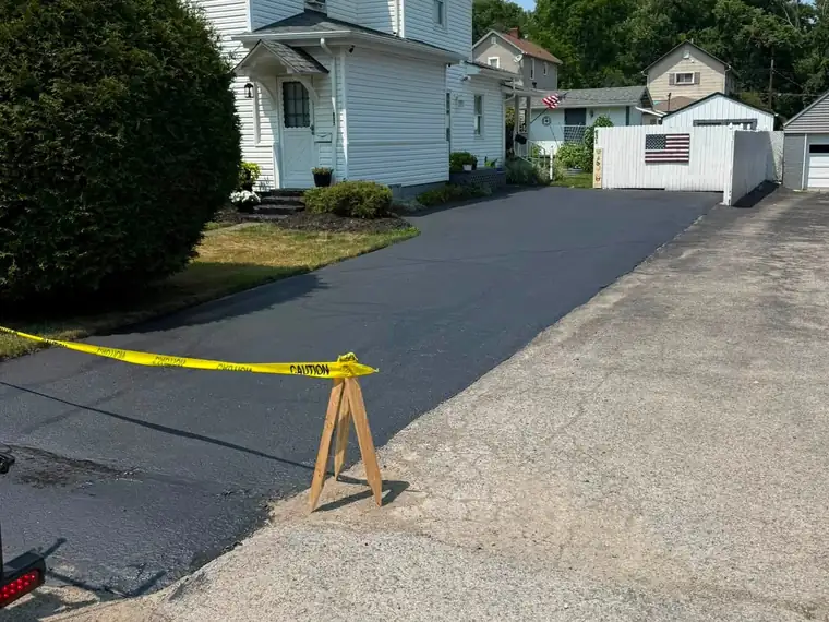 Freshly sealed asphalt driveway alongside a white house
