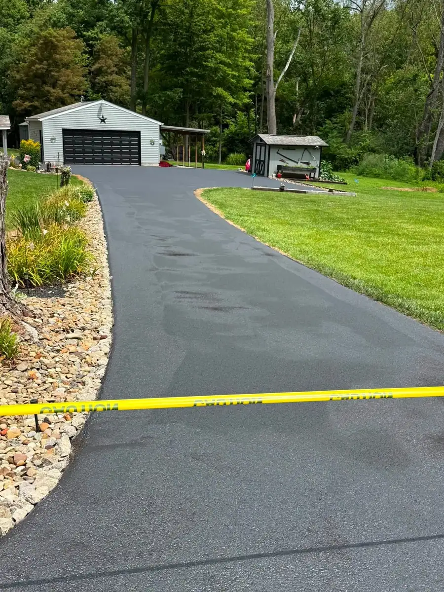 A curved residential driveway finished in deep black sealcoat, with stone edging and a dark garage door