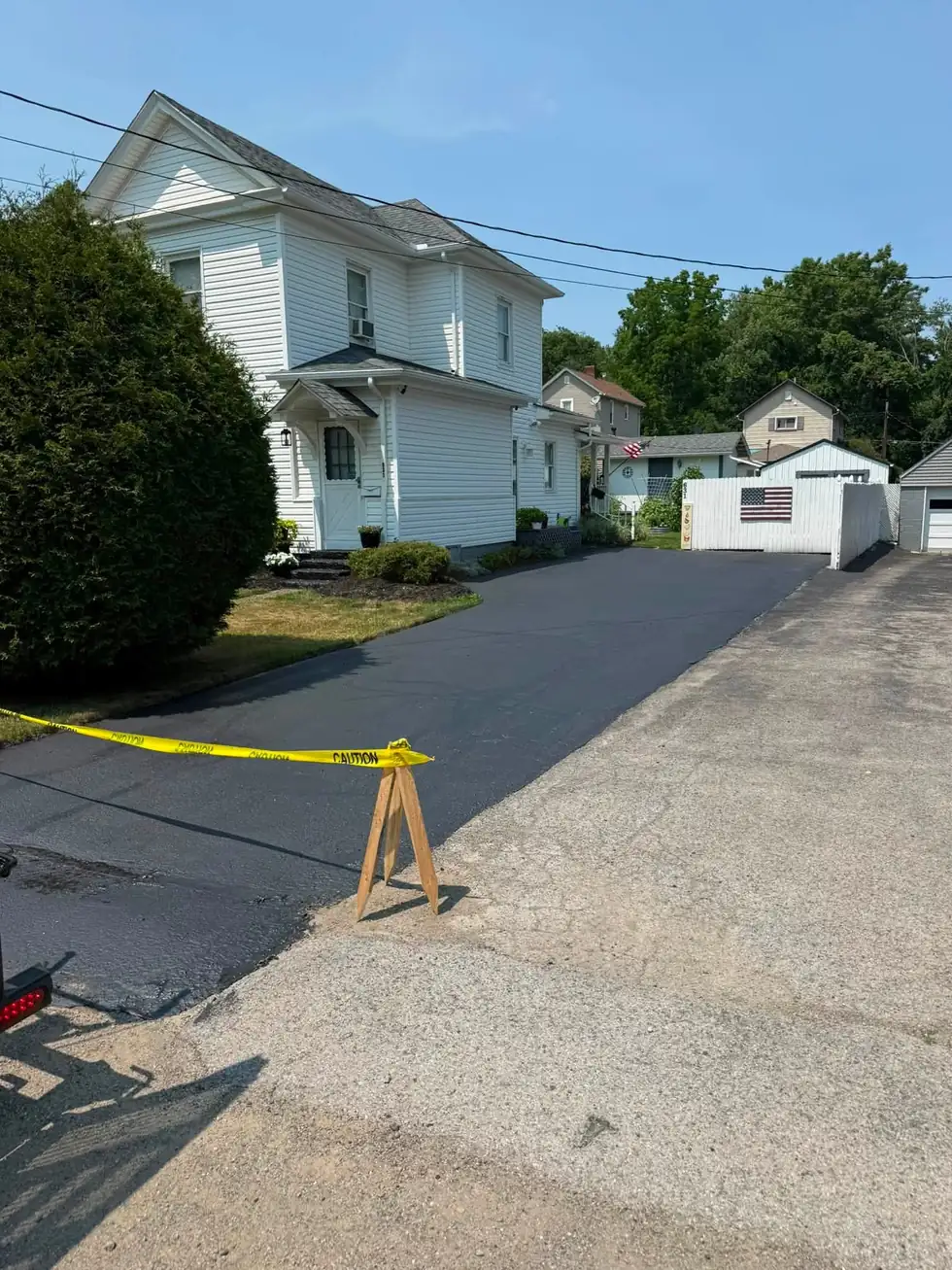 A freshly sealed driveway running alongside a white house