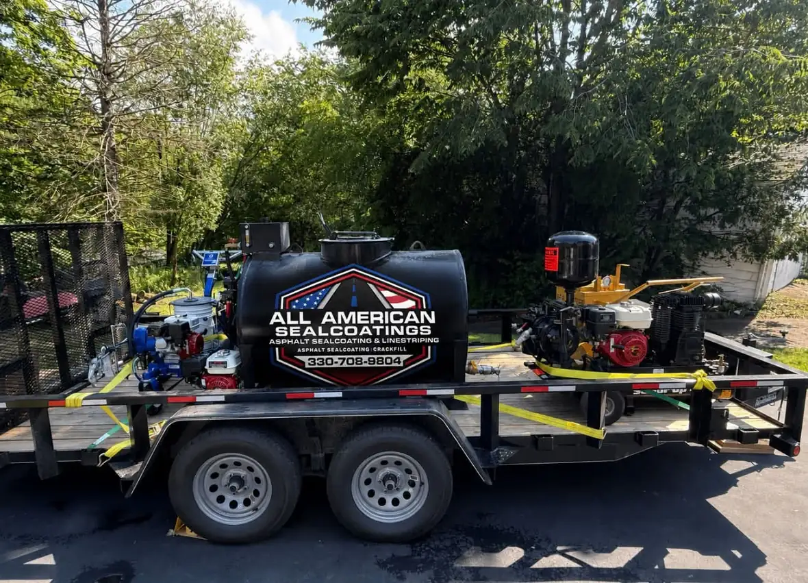 The All American Sealcoatings branded trailer and sealer tank on a job site